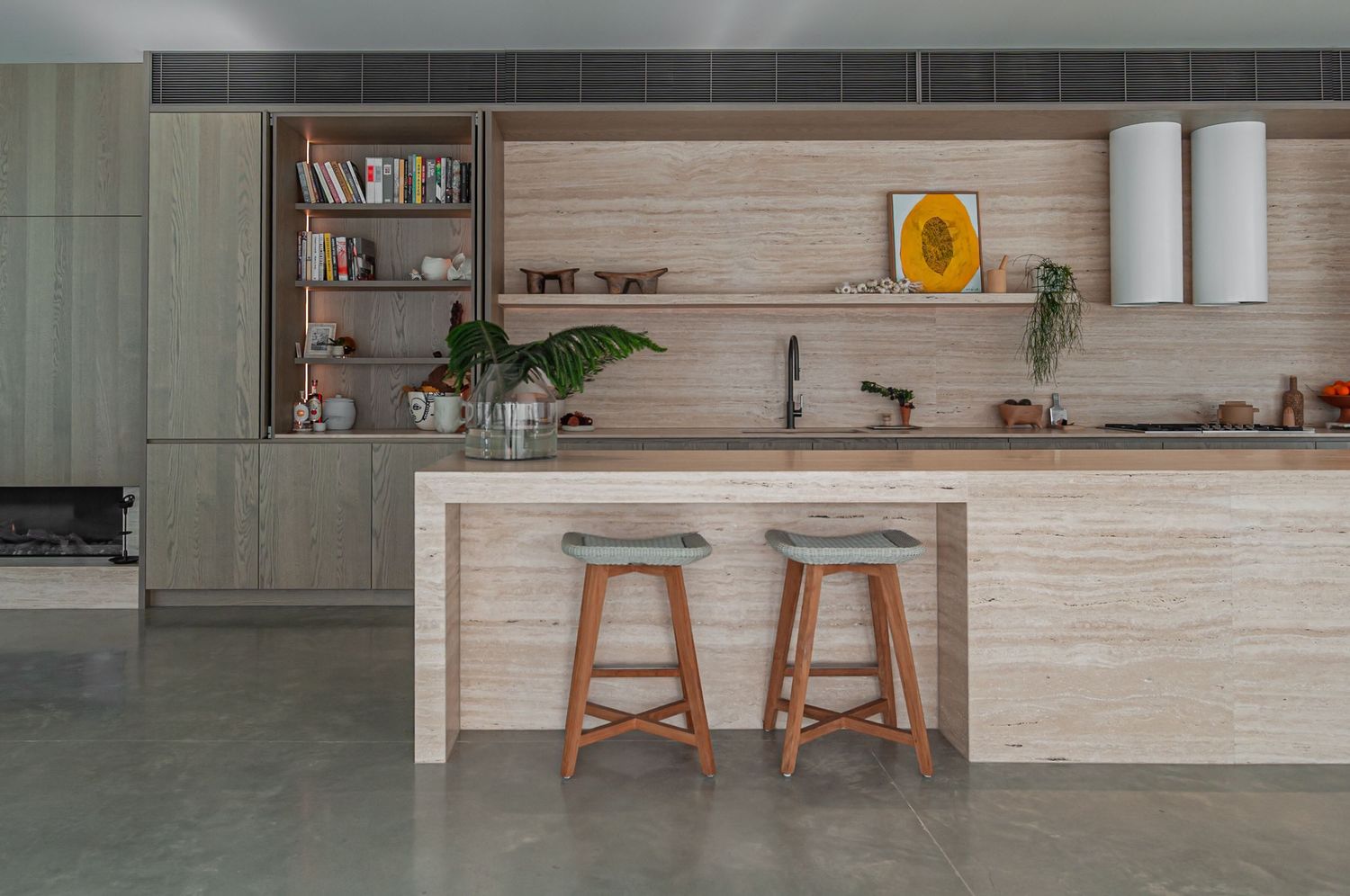 Modern minimalist kitchen with wooden bar stools, light wood paneling, and open shelving displays a clean design aesthetic.