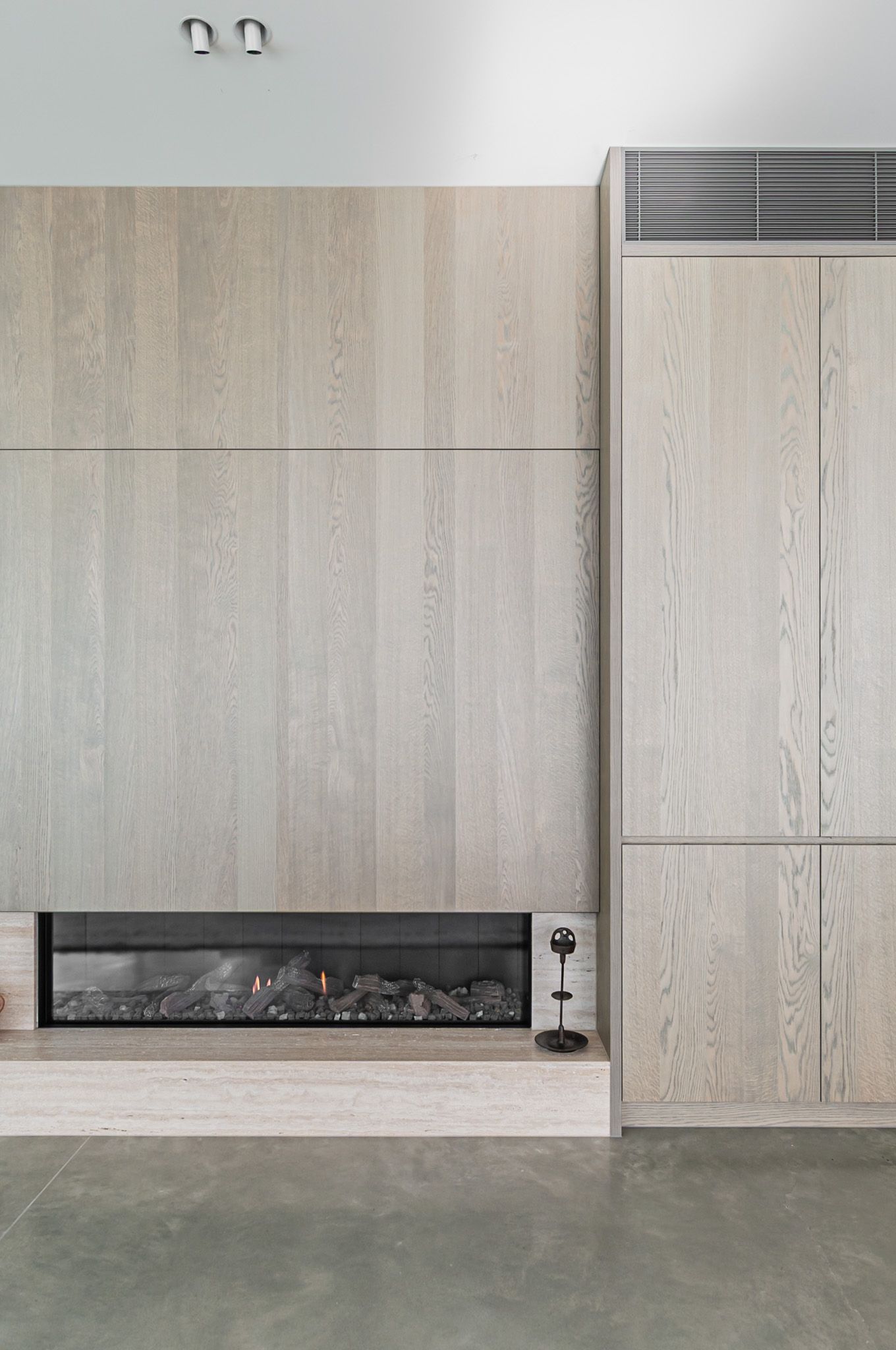Modern sleek linear fireplace installed in light wood paneled wall with concrete floor provides contemporary minimalist design.