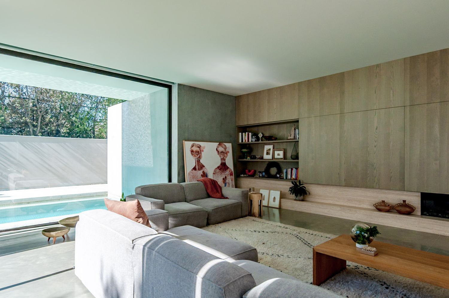 Modern minimalist living room features concrete walls, large windows, and wooden furniture in a sleek open layout design.