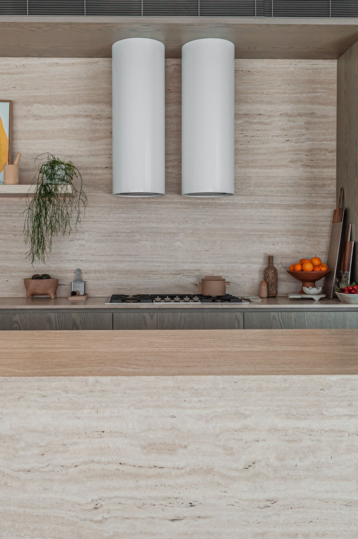 Contemporary kitchen featuring dual white cylinder range hoods, gas stovetop, and natural wood accents.