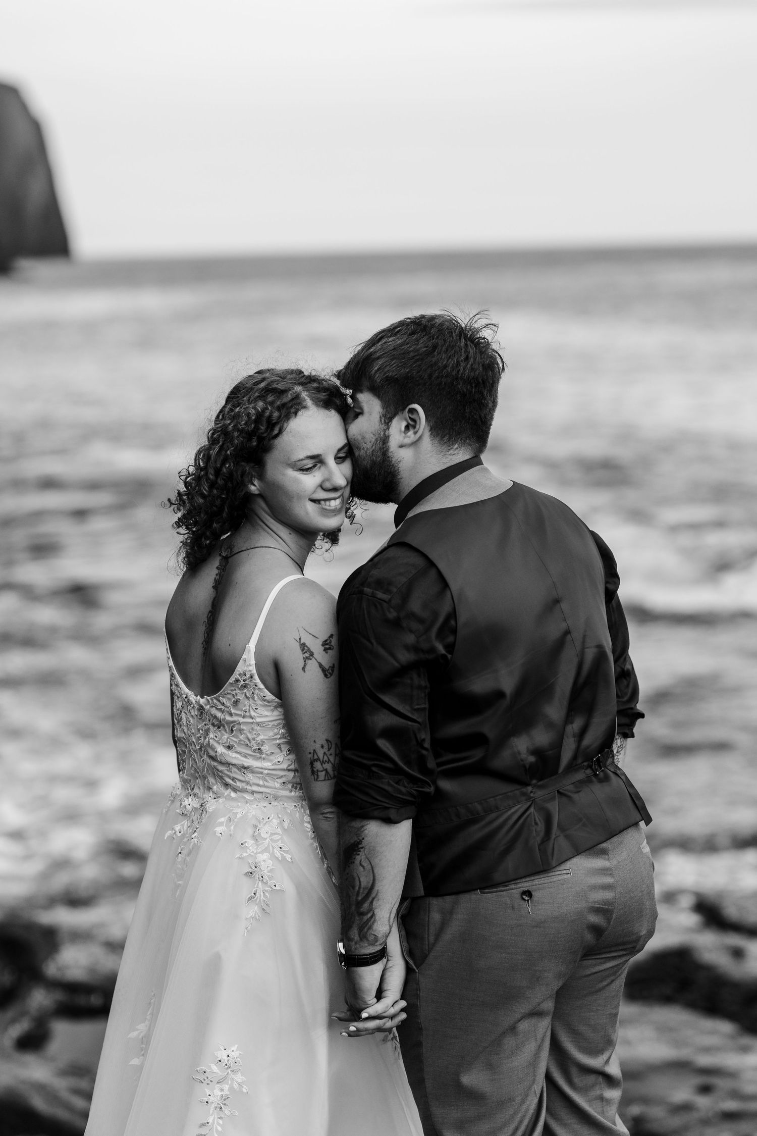 A romantic black and white series of a couple embracing on a rocky beach as waves crash in the background.