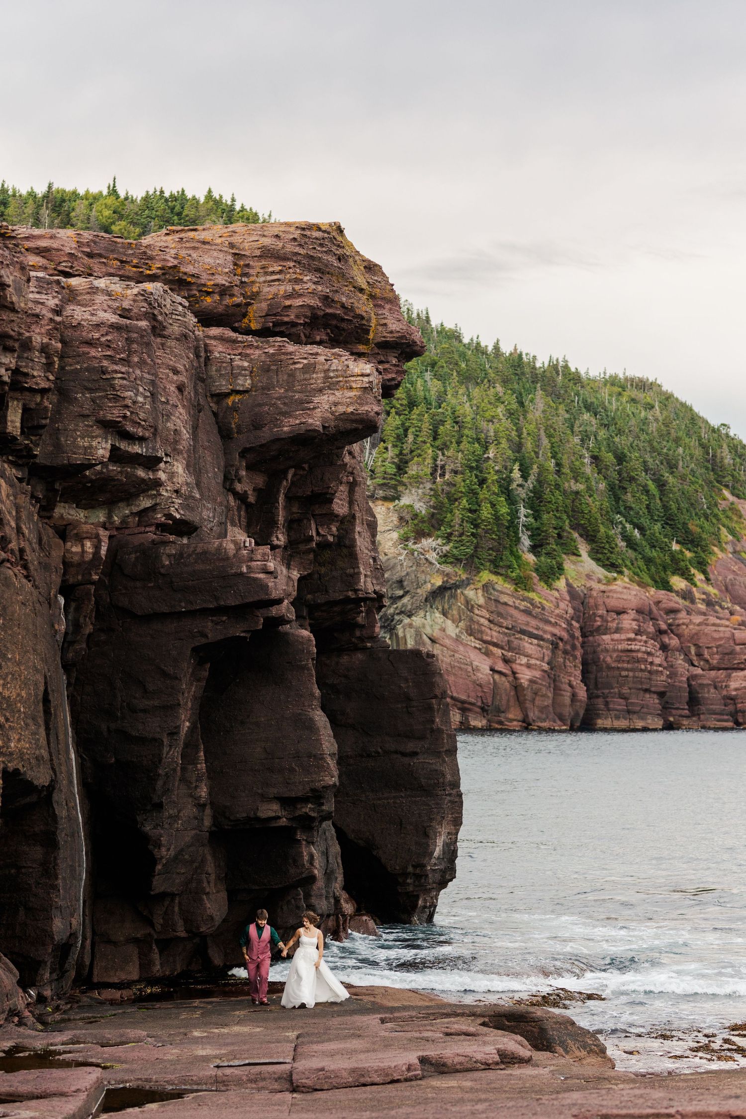 A couple shares an intimate moment along the rugged sea caves and cliffs at a coastal wedding venue.