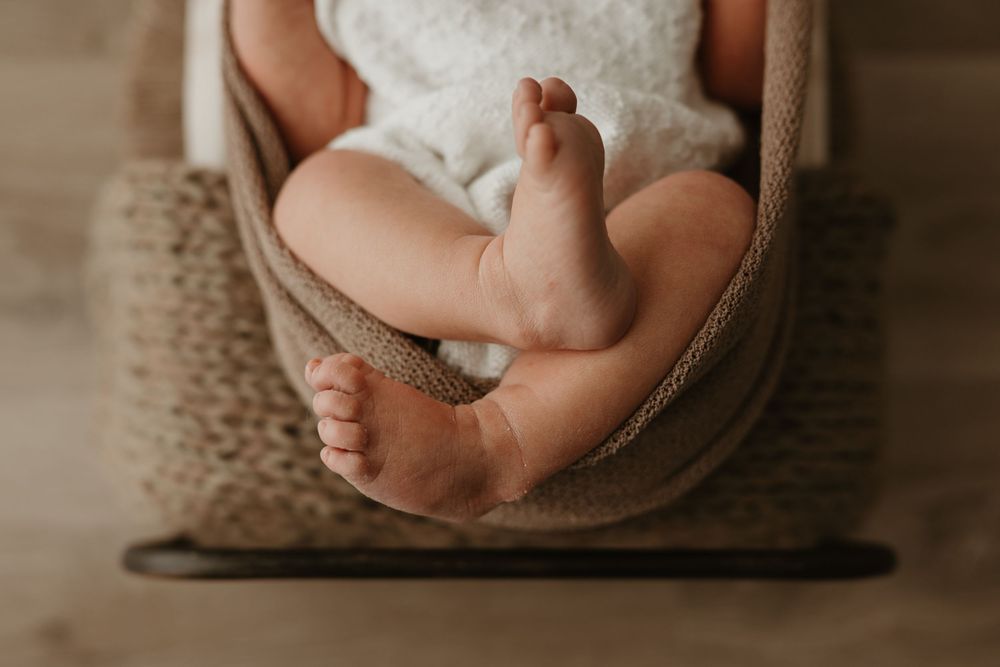 Close-up of a newborn baby's tiny feet and legs resting in a cozy knit hammock during a newborn photography session.
Regina newborn