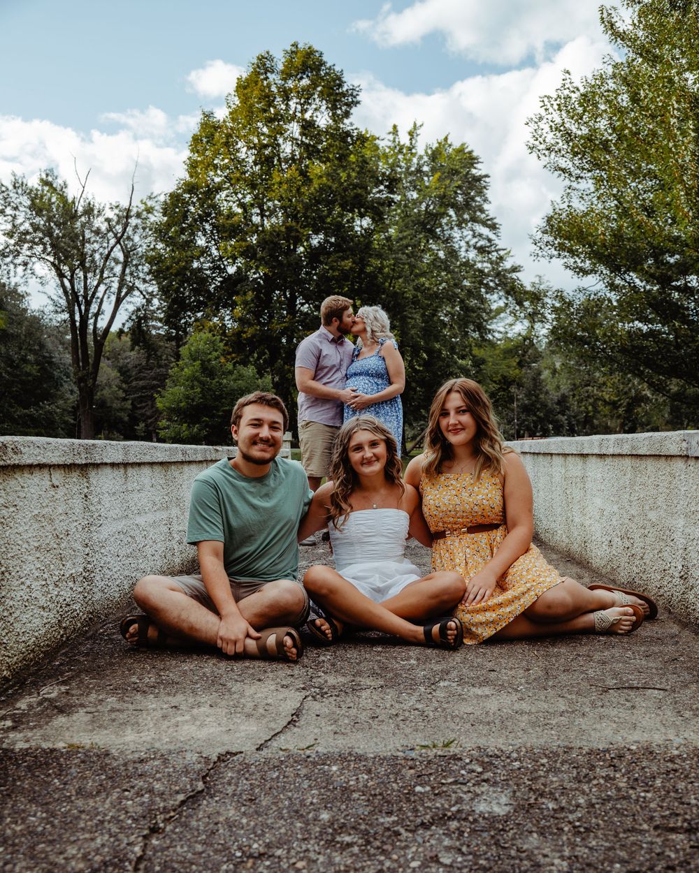A group of friends sitting together on a concrete wall outdoors on a sunny summer day.