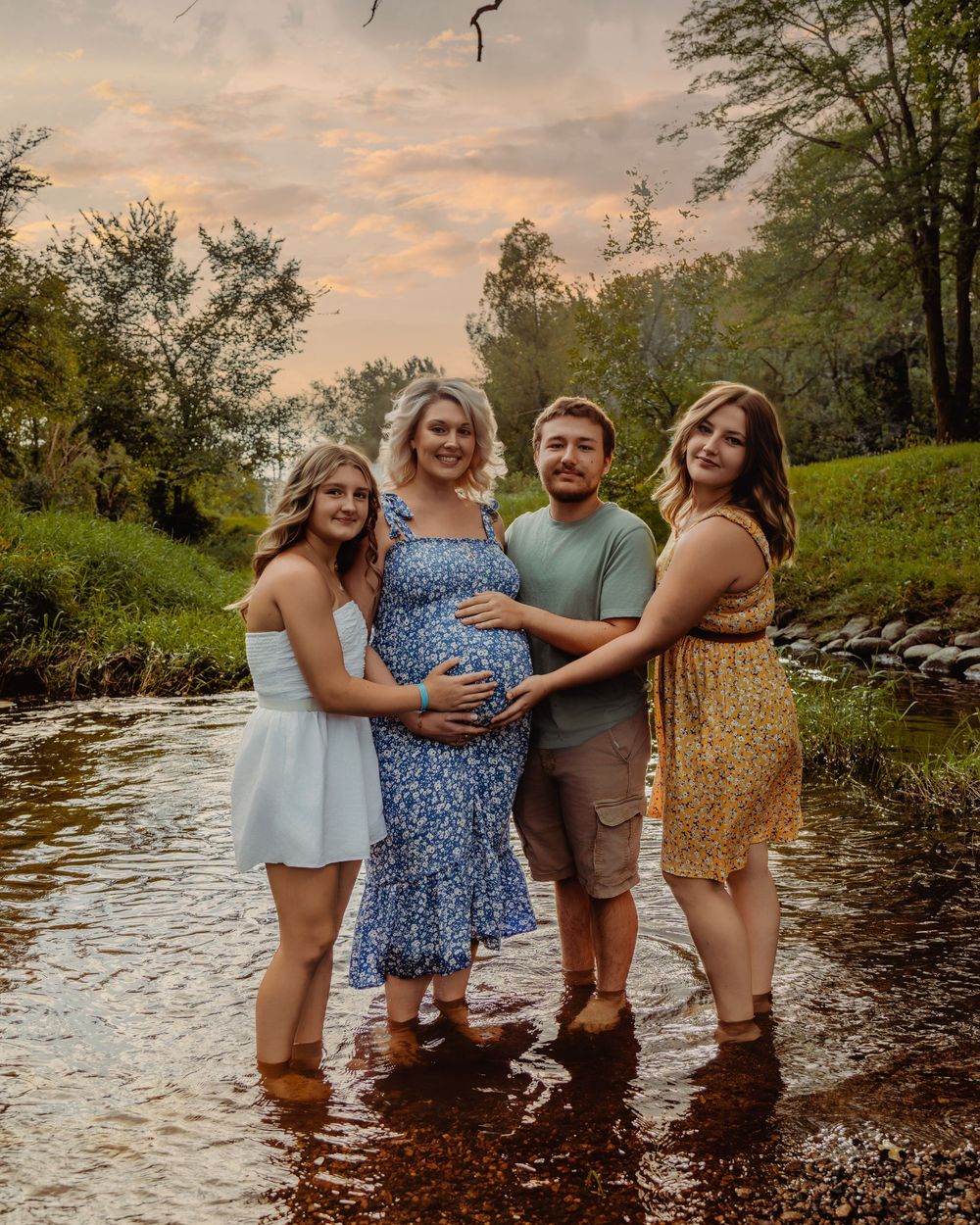 A group poses in a creek at sunset as they gather together for a maternity photoshoot in nature.