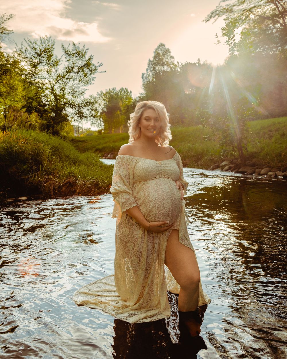 A sunset maternity photoshoot in a flowing stream creates a dreamy, ethereal atmosphere in warm golden light.