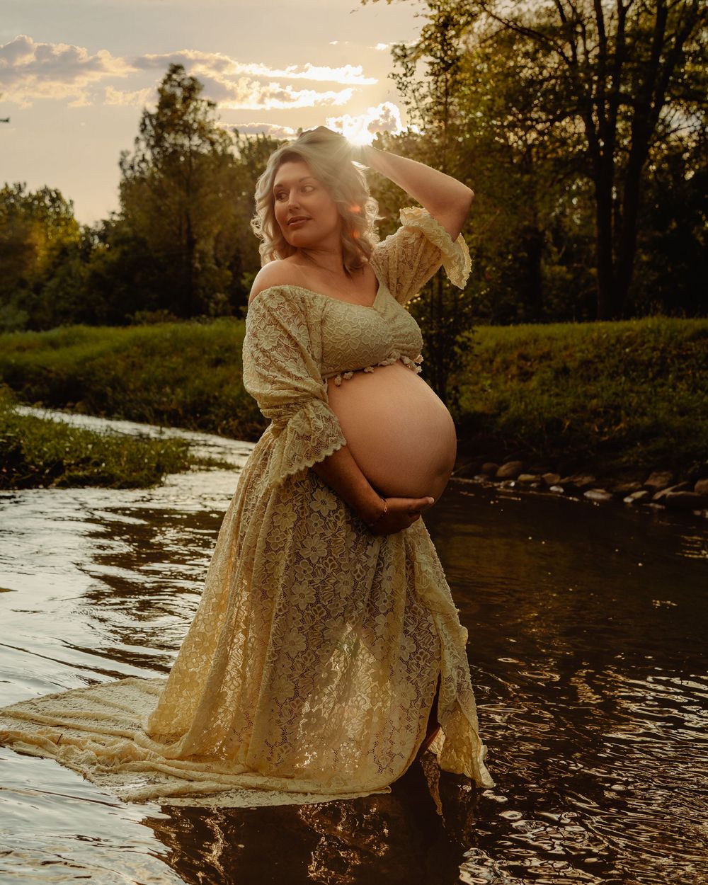 Person in gold dress stands gracefully by river at sunset creating ethereal reflections in flowing water.