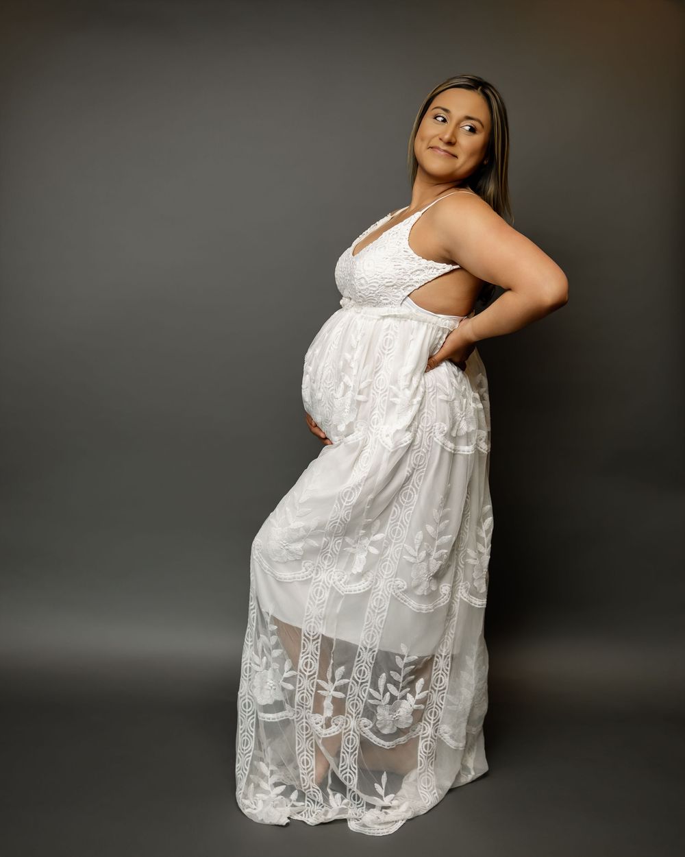 A series of maternity photos showing a woman in a white lace dress posing elegantly against a dark backdrop.