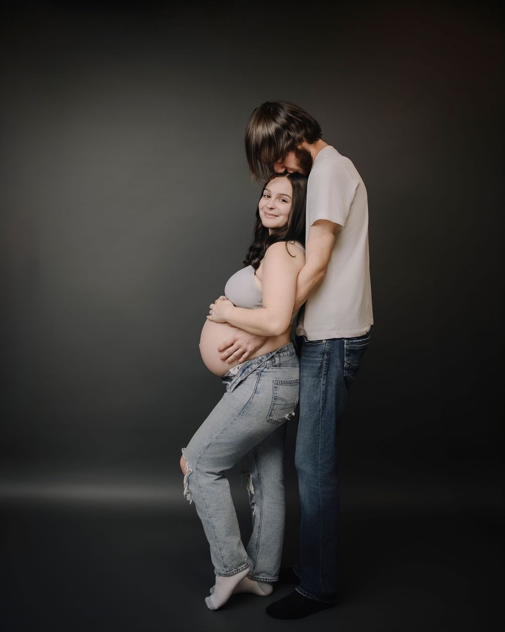 A tender embrace captured in a series of moody black and white studio photos against a dark background.