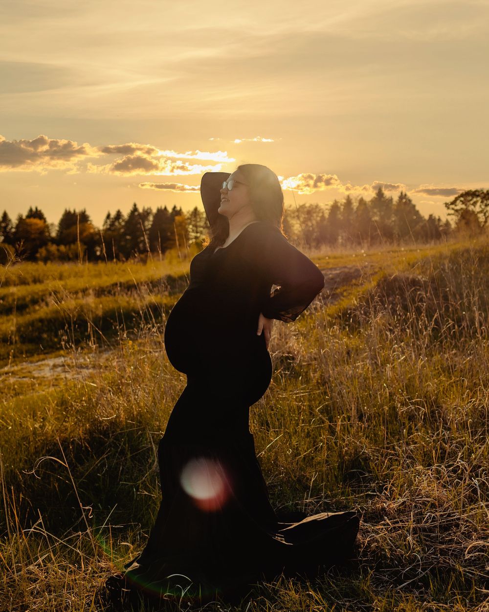 A silhouetted figure sits on grassy terrain against a golden sunset sky with lens flares and dramatic lighting.