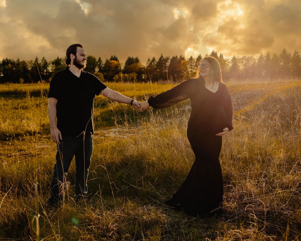 Silhouetted couple dances in a golden meadow at sunset while sun rays illuminate tall grasses behind them.