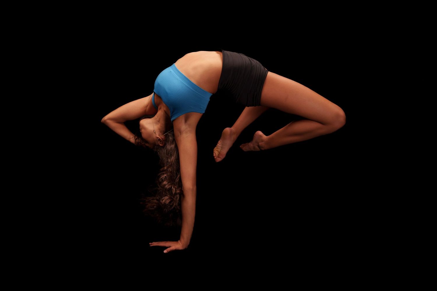 Artistic silhouette of gymnast performing acrobatic moves against dark background.