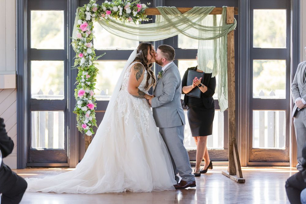 A beautiful wedding ceremony takes place under a floral arch inside an elegant venue with large windows.