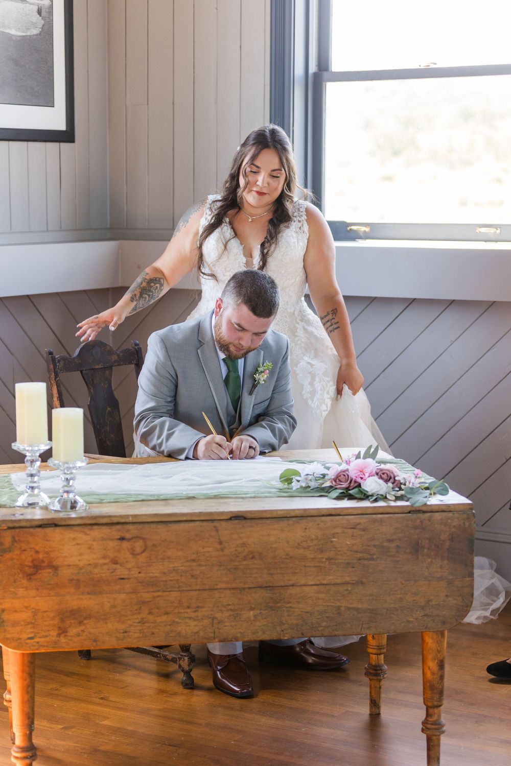 A couple signs their marriage license at a wooden table decorated with flowers and candles during an intimate ceremony.