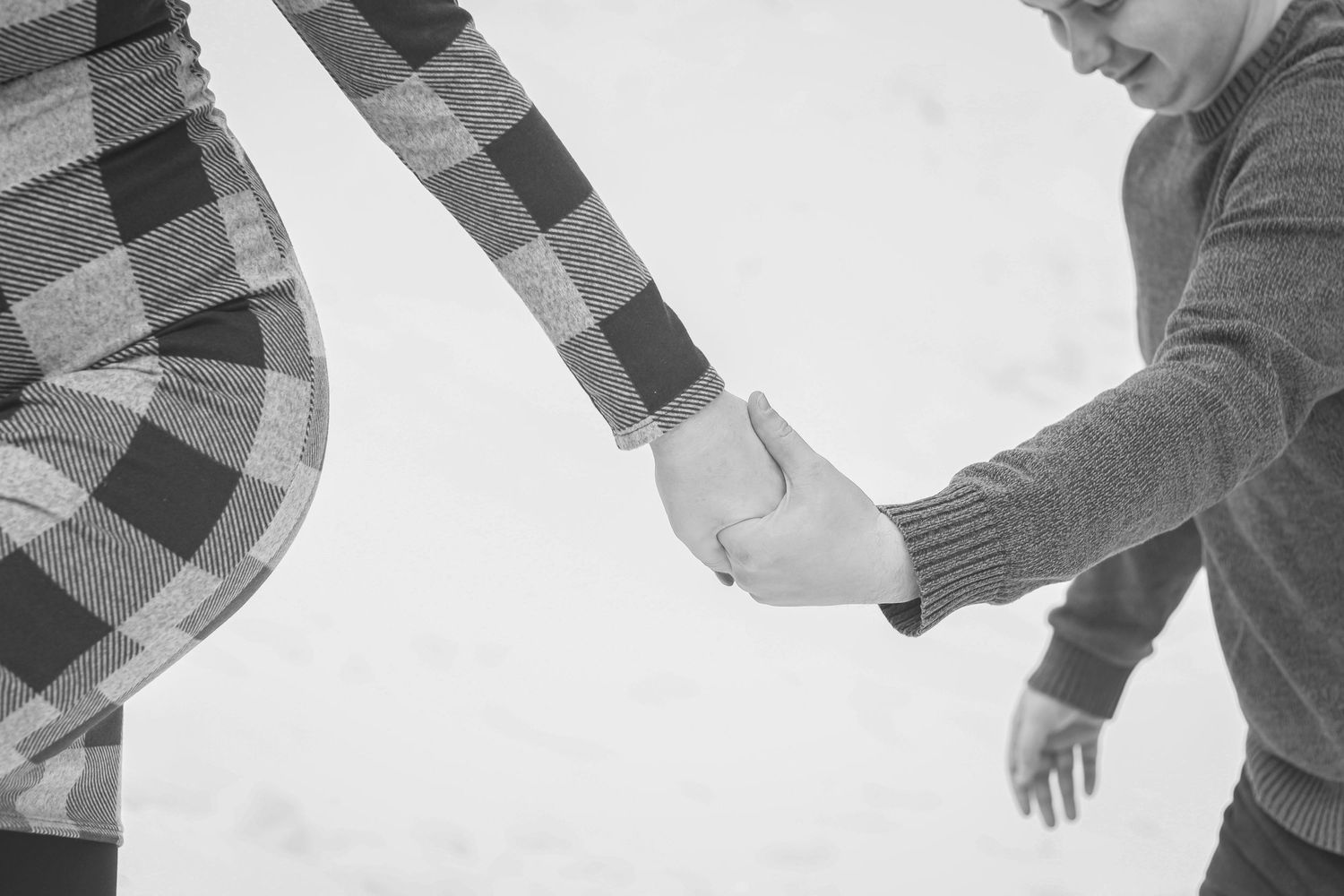 A black and white close-up of a couple holding hands in a snowy outdoor setting.