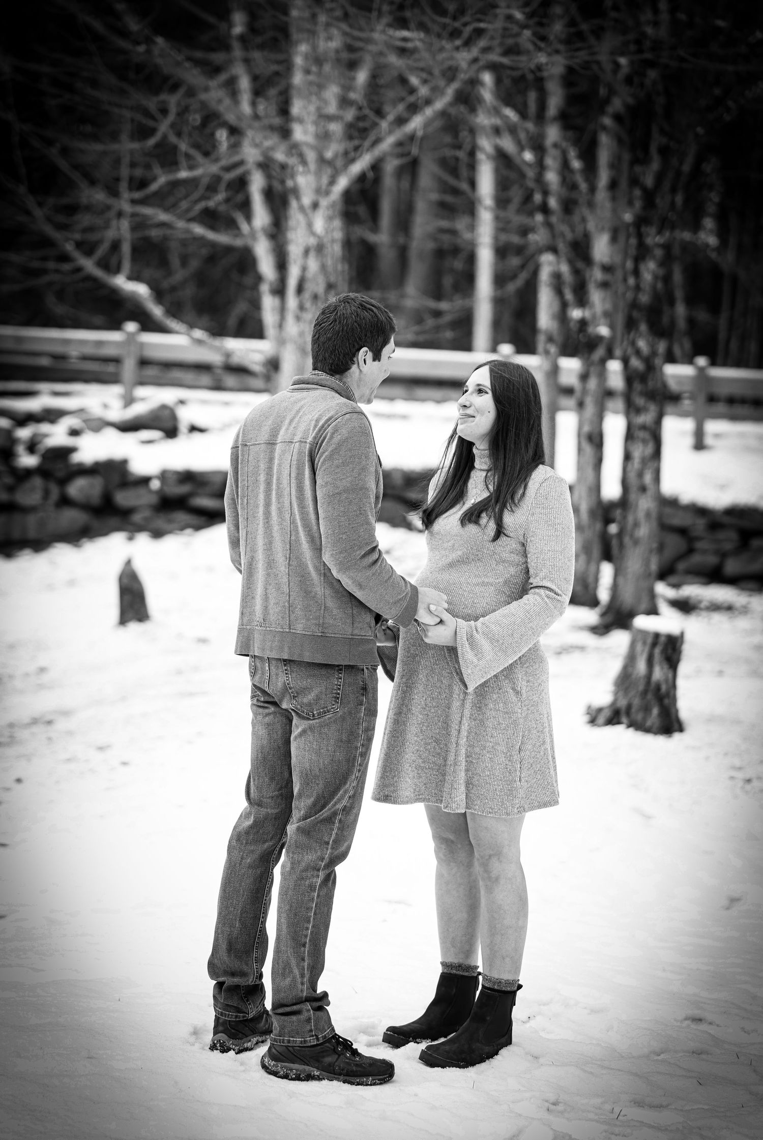 Couple holding hands and gazing at each other in a snowy winter forest setting.