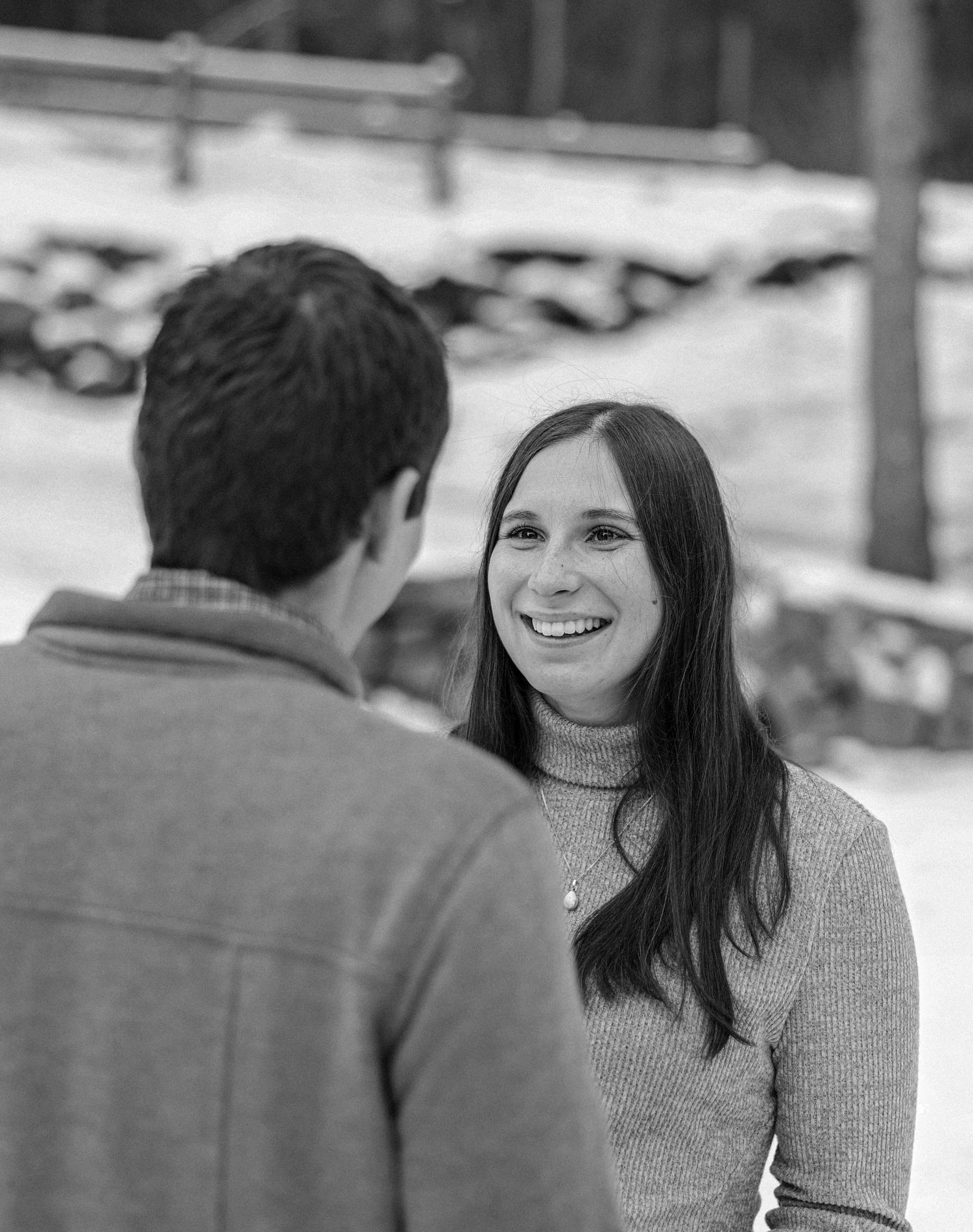 Smiling woman with long dark hair looking at partner in snowy outdoor winter setting.