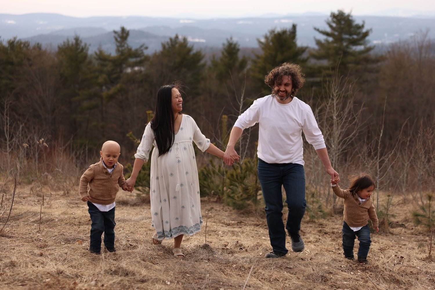Joyful family with pregnant mother, father, and two children walking hand in hand outdoors.