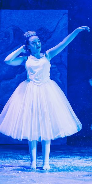 A ballerina in a white tutu performs under blue stage lighting during a dance recital.