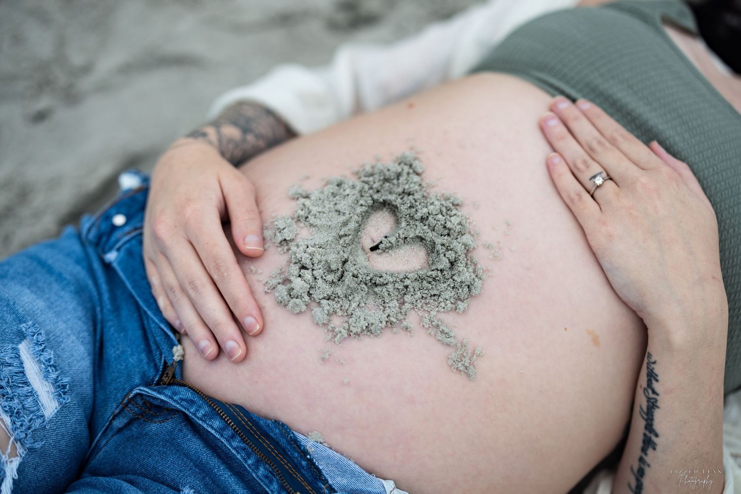 A pregnant woman lying down with a sand heart shape decorating her bare baby bump.