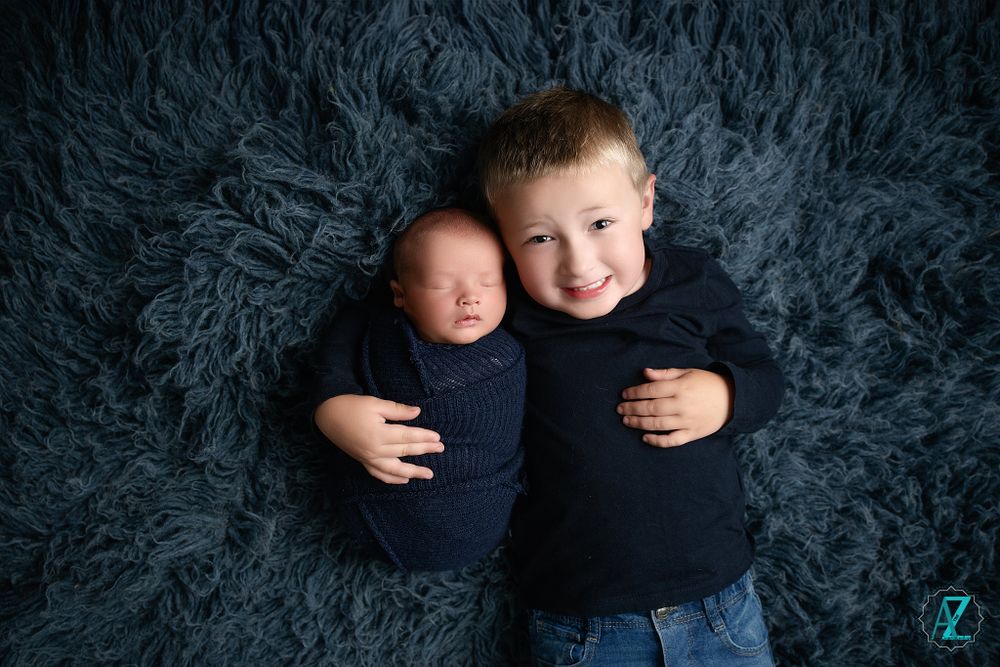 Heartwarming sibling portrait on dark gray fur rug showing loving embrace.