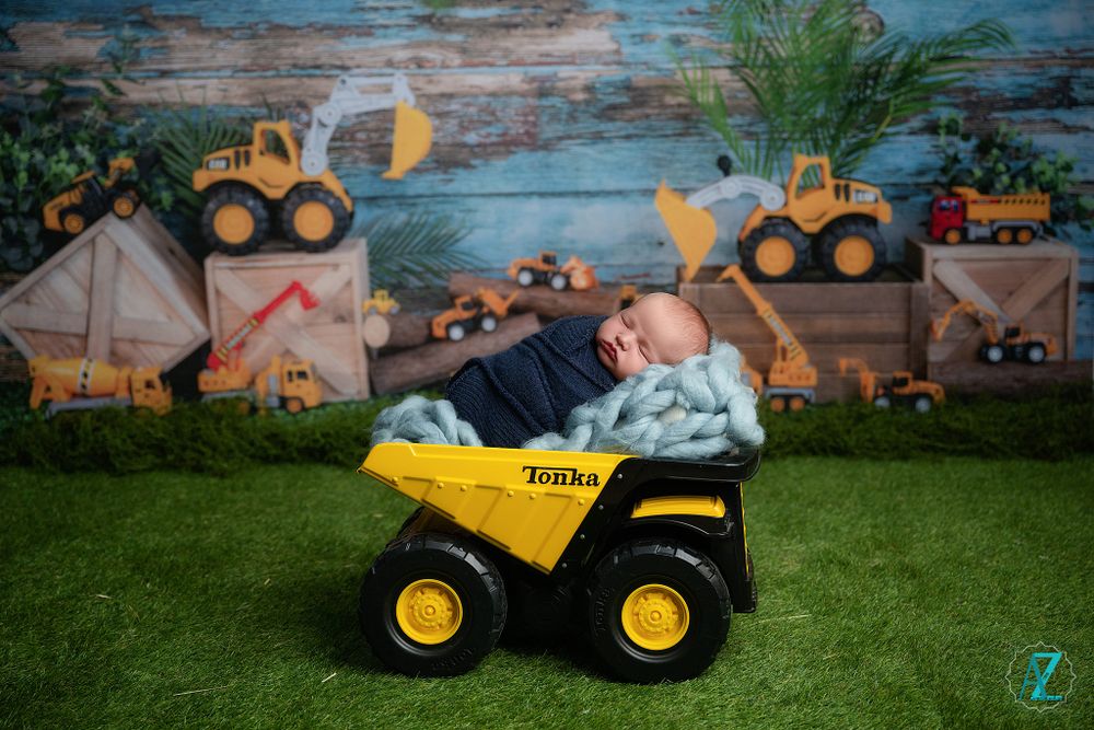 Creative newborn photo with toy construction vehicles and rustic wooden backdrop.