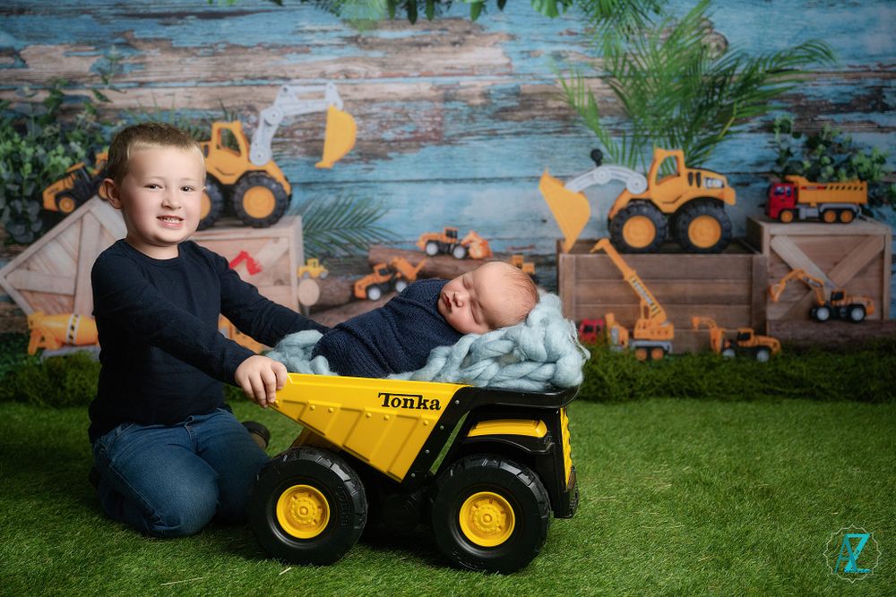Children pose with yellow toy dump truck against construction-themed backdrop with decorative elements.