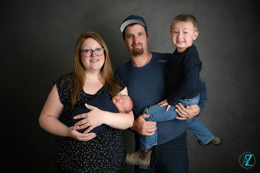 Family portrait of four people against dark background wearing coordinating blue and black outfits.