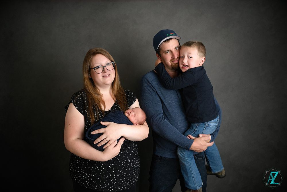 Family of four poses together against dark grey background in casual attire.