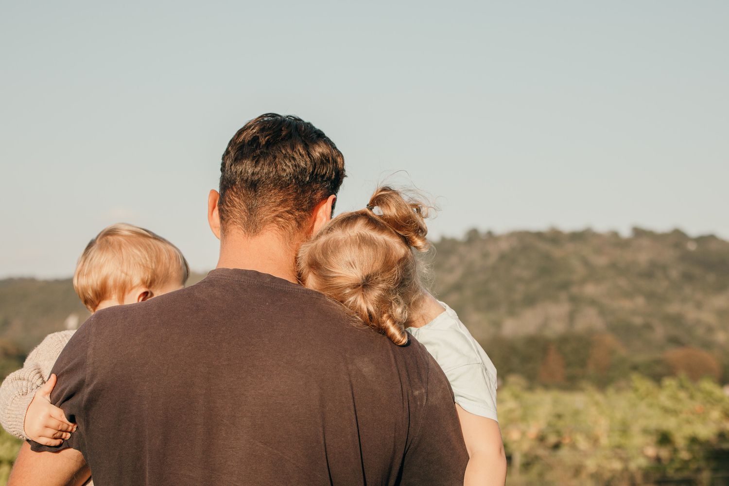 Person holding two children while overlooking a scenic mountain landscape.