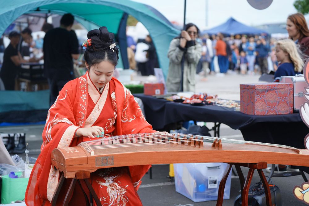 Candid event photography of a musician playing Guzheng in traditional Hanfu at the Dragon Boat Festival, by an Auckland photographer.