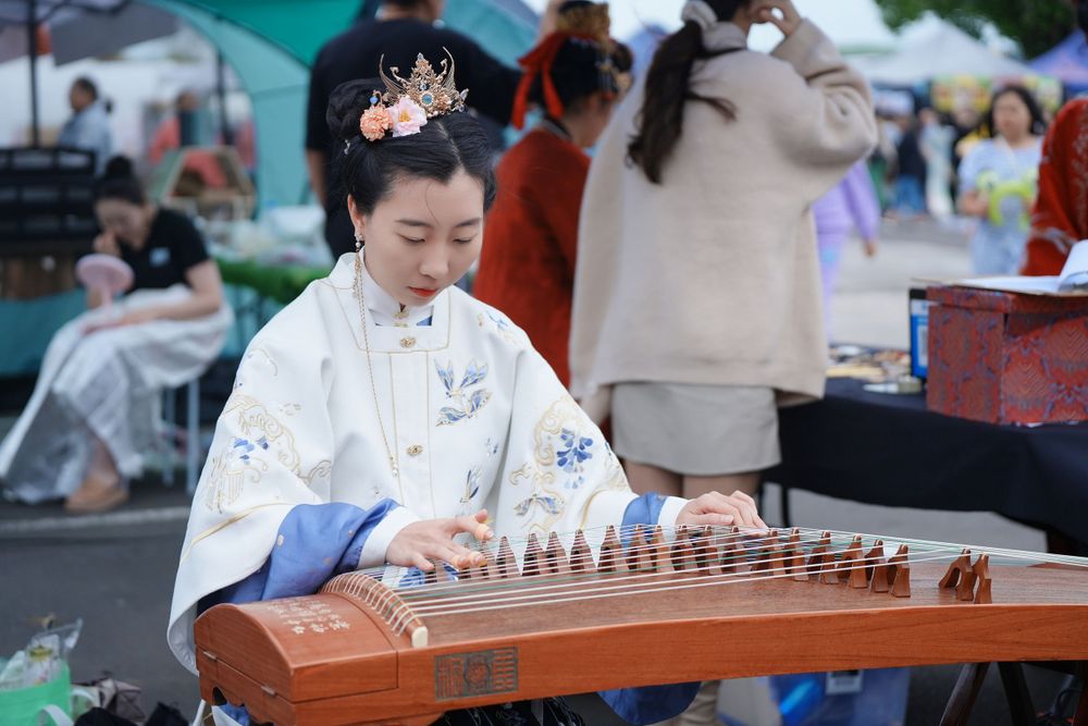 Candid event photography of a musician playing Guzheng in traditional Hanfu at the Dragon Boat Festival, by an Auckland photographer.