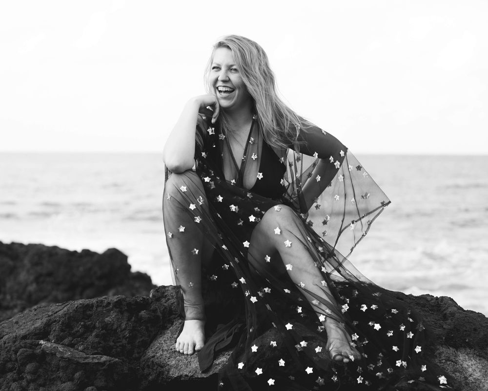 Joyful portrait in polka dot dress on oceanside rocks.