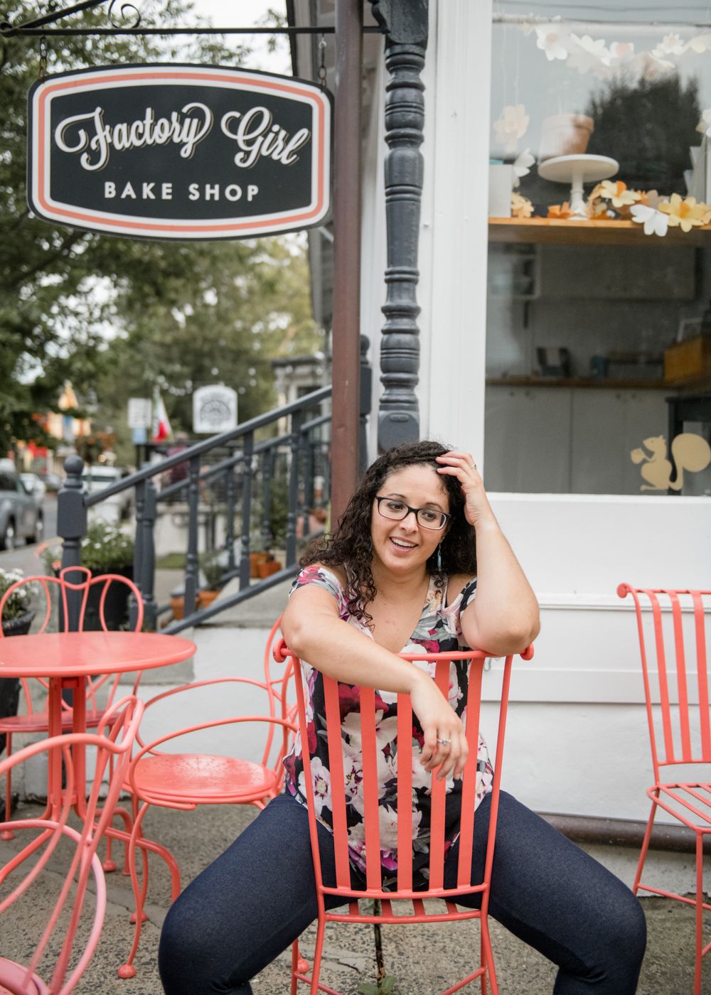 Person sitting in coral-colored chair outside Factory Girl Bake Shop.
