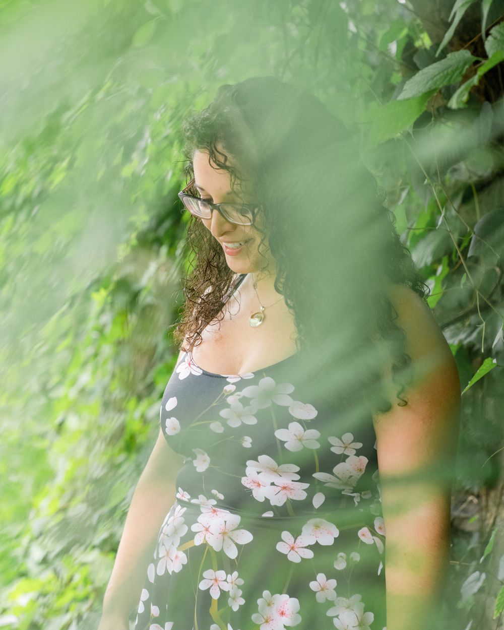 Dreamy portrait through green foliage wearing floral dress.