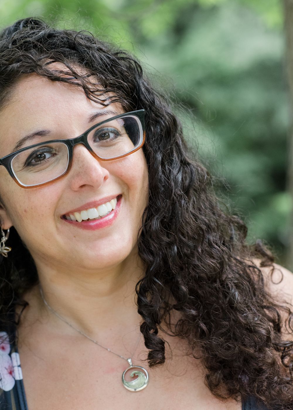Close-up portrait wearing glasses with curly hair and pendant necklace.