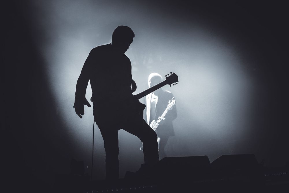 Silhouette of a guitarist performing on stage with dramatic backlighting creating a moody atmospheric effect.