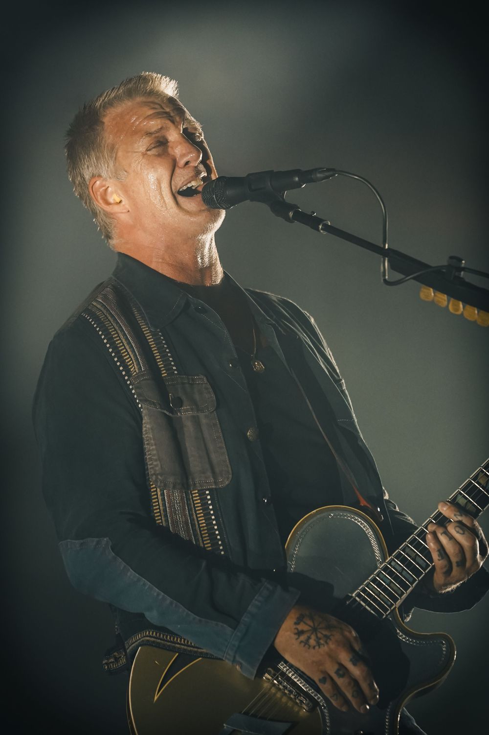 A performer sings passionately while playing acoustic guitar on a dimly lit stage during an emotional musical performance.