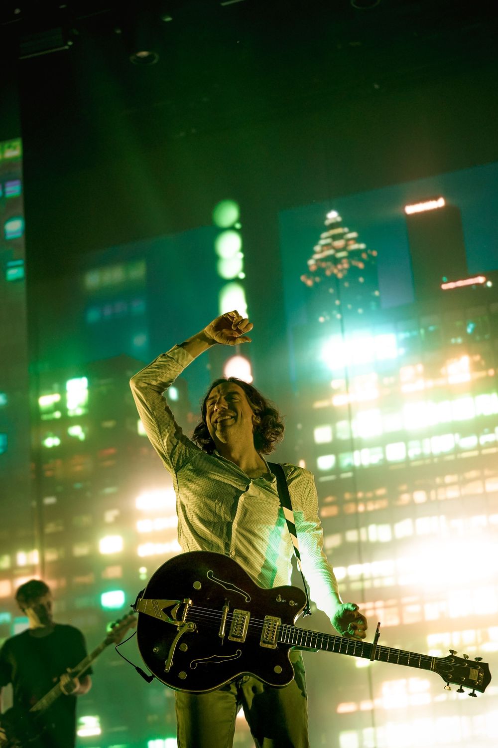 Musicians perform on stage with dramatic green lighting and smoke effects during a rock concert.