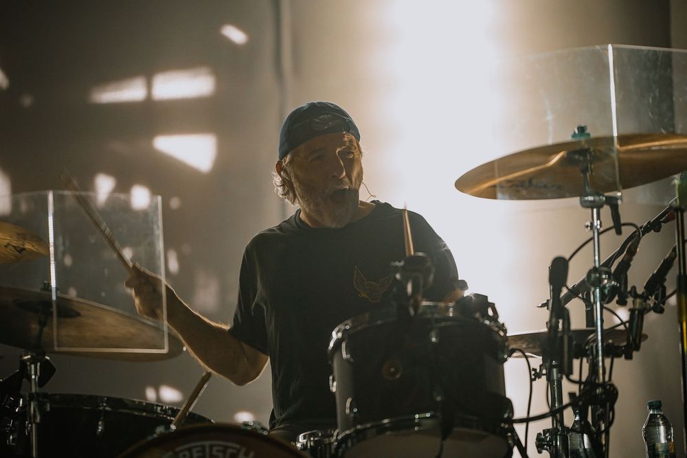 Silhouetted drummer performing on stage with dramatic lighting and cymbals visible.