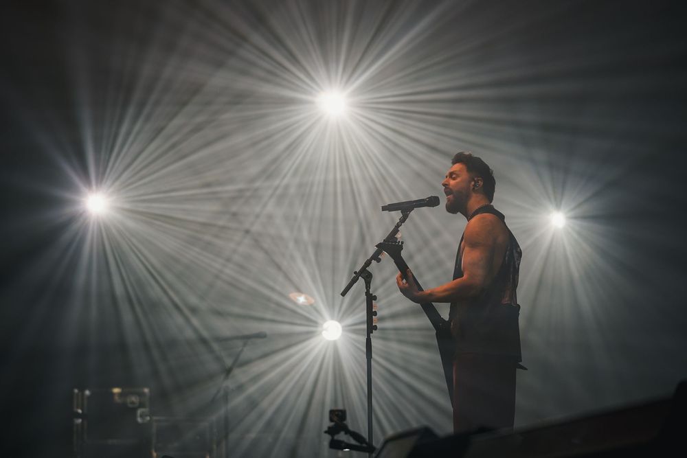 A silhouetted performer sings on stage with dramatic starburst lighting effects creating an atmospheric concert scene.