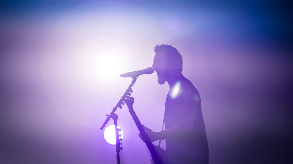 Silhouetted performers on stage with dramatic purple lighting during a live concert performance.