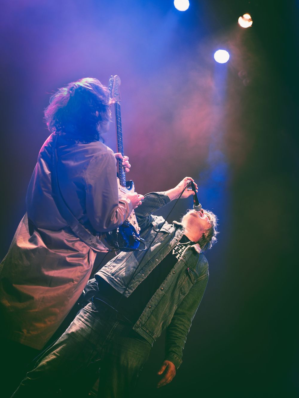 Musicians perform on stage with dramatic purple and blue lighting creating an atmospheric concert environment.