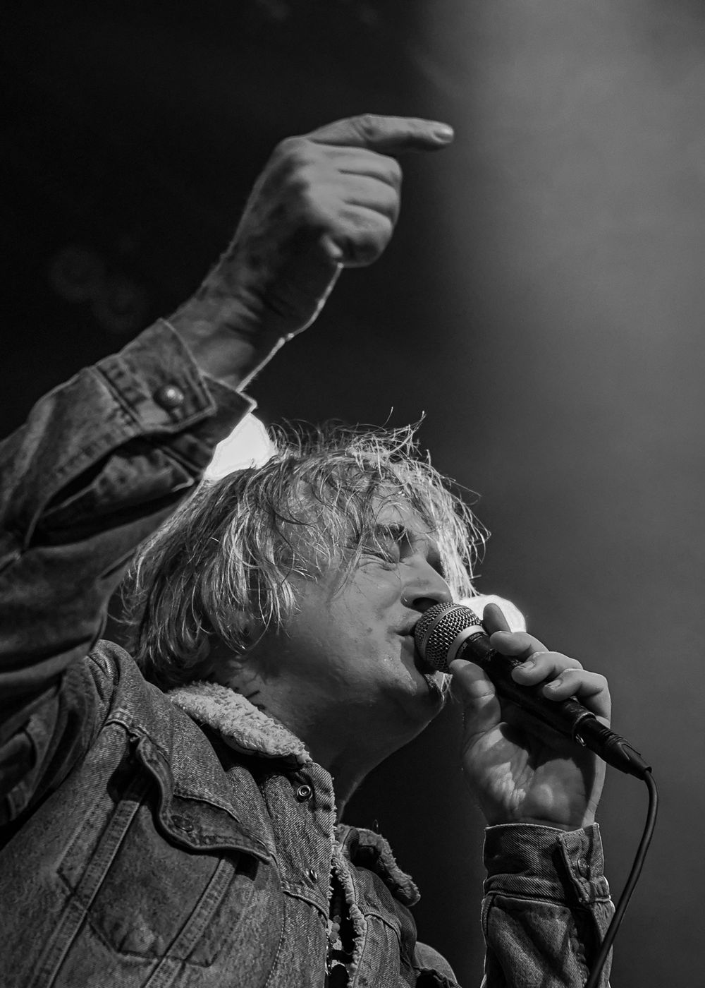 Black and white shot of a performer singing passionately into a microphone during a concert.