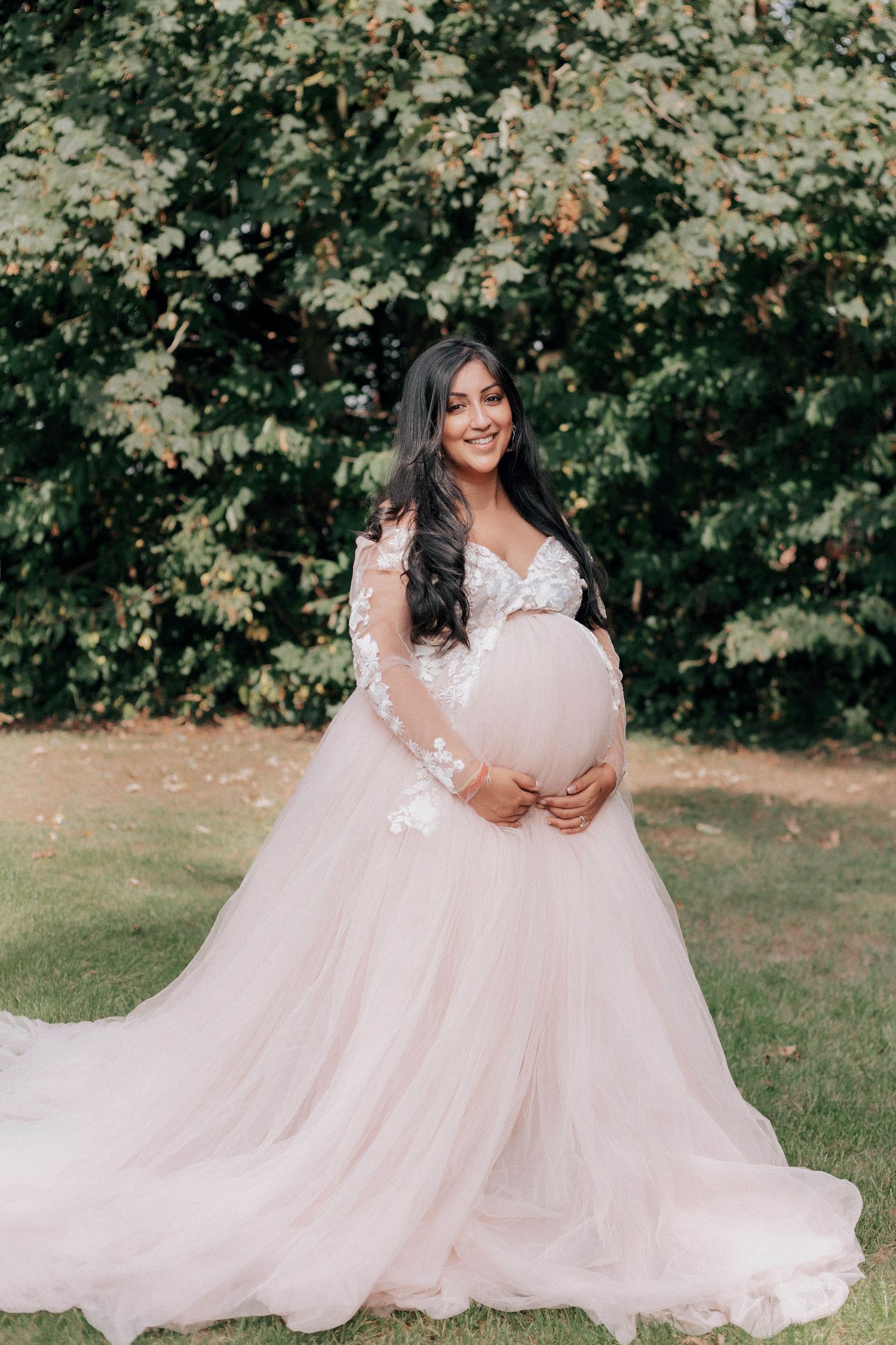 Ethereal outdoor maternity session featuring flowing pink gown and natural garden backdrop.