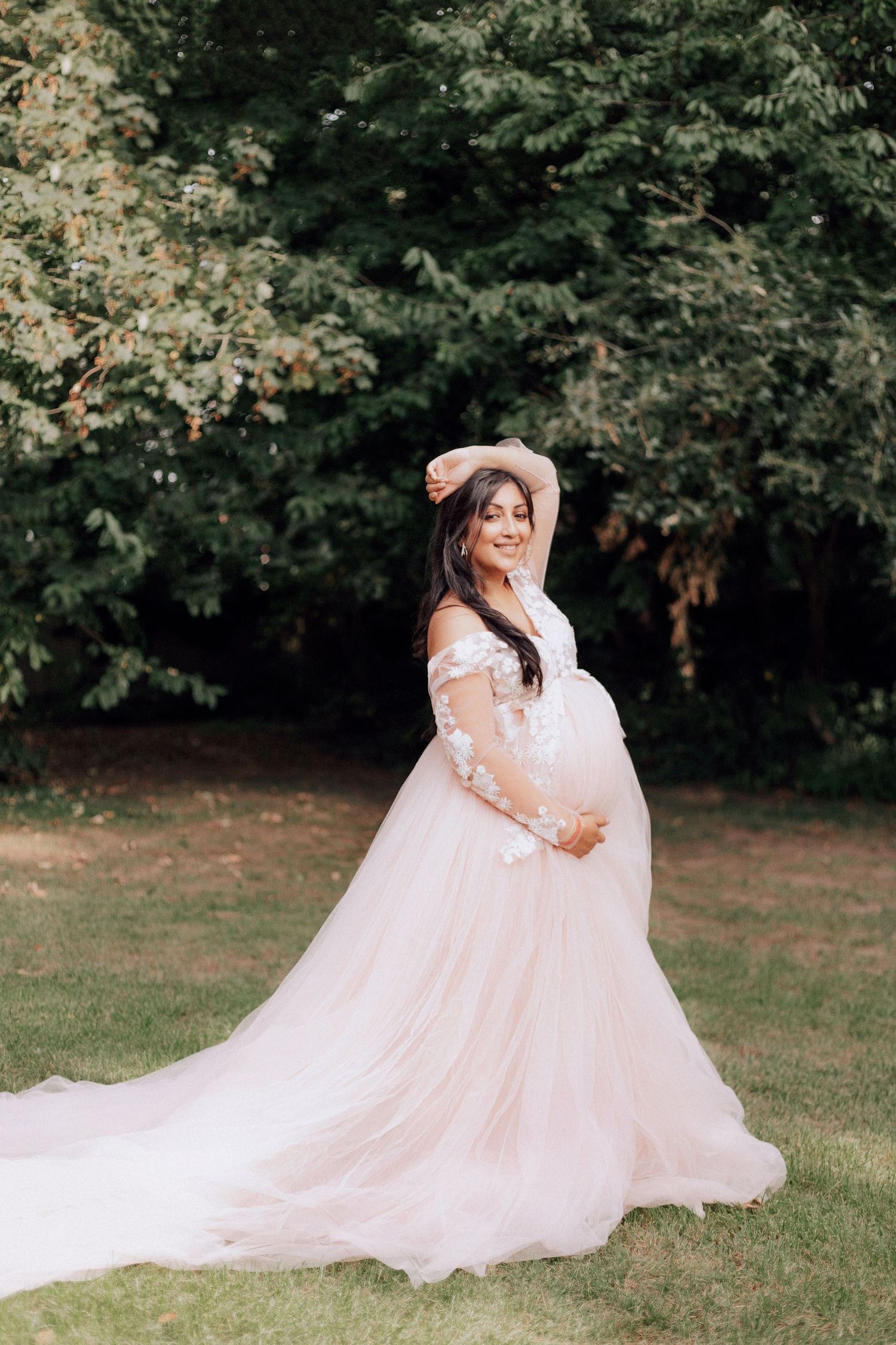 Ethereal maternity photos in a flowing pink gown outdoors.
