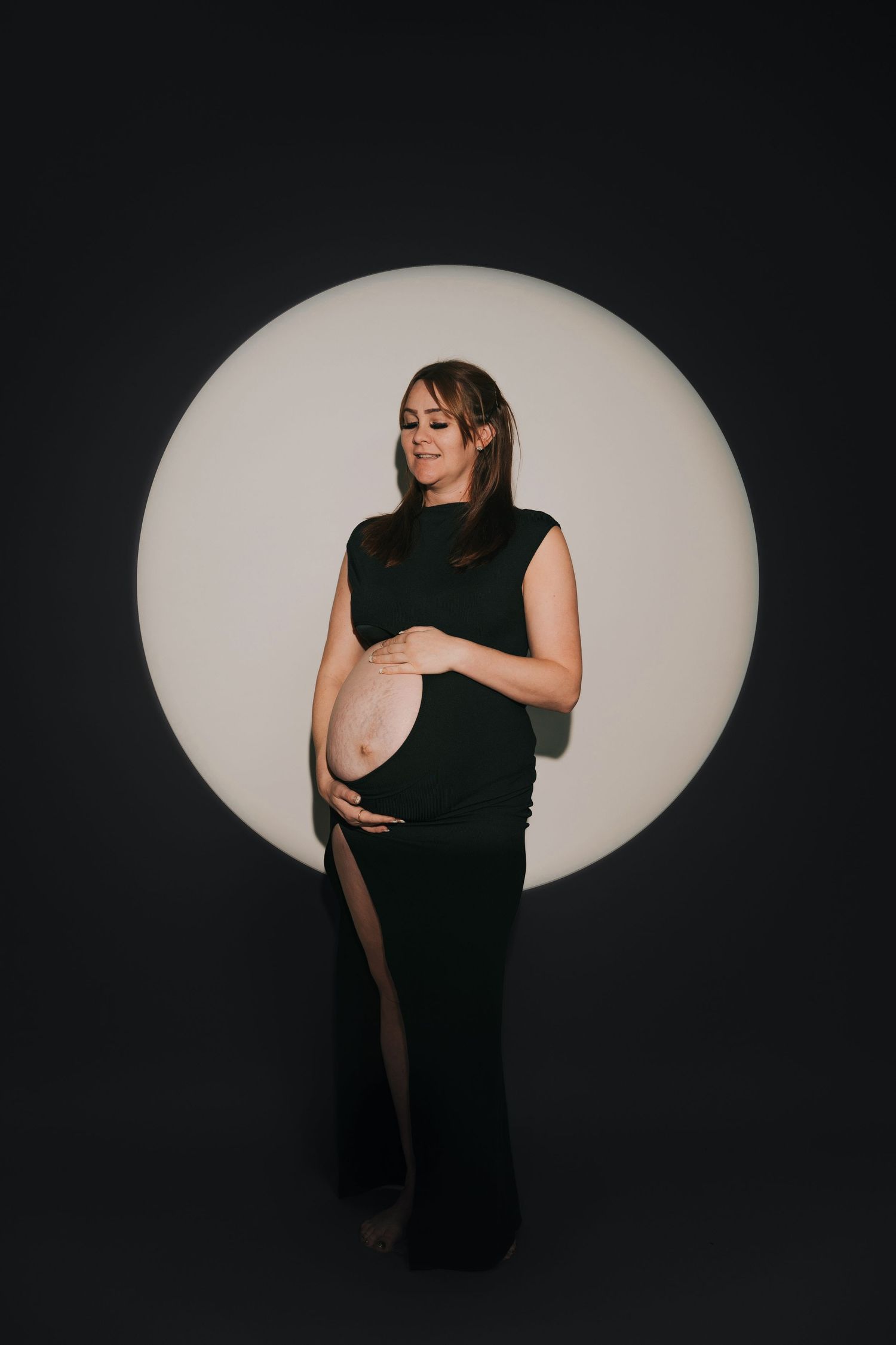 Artistic maternity silhouettes against oval light backdrop.