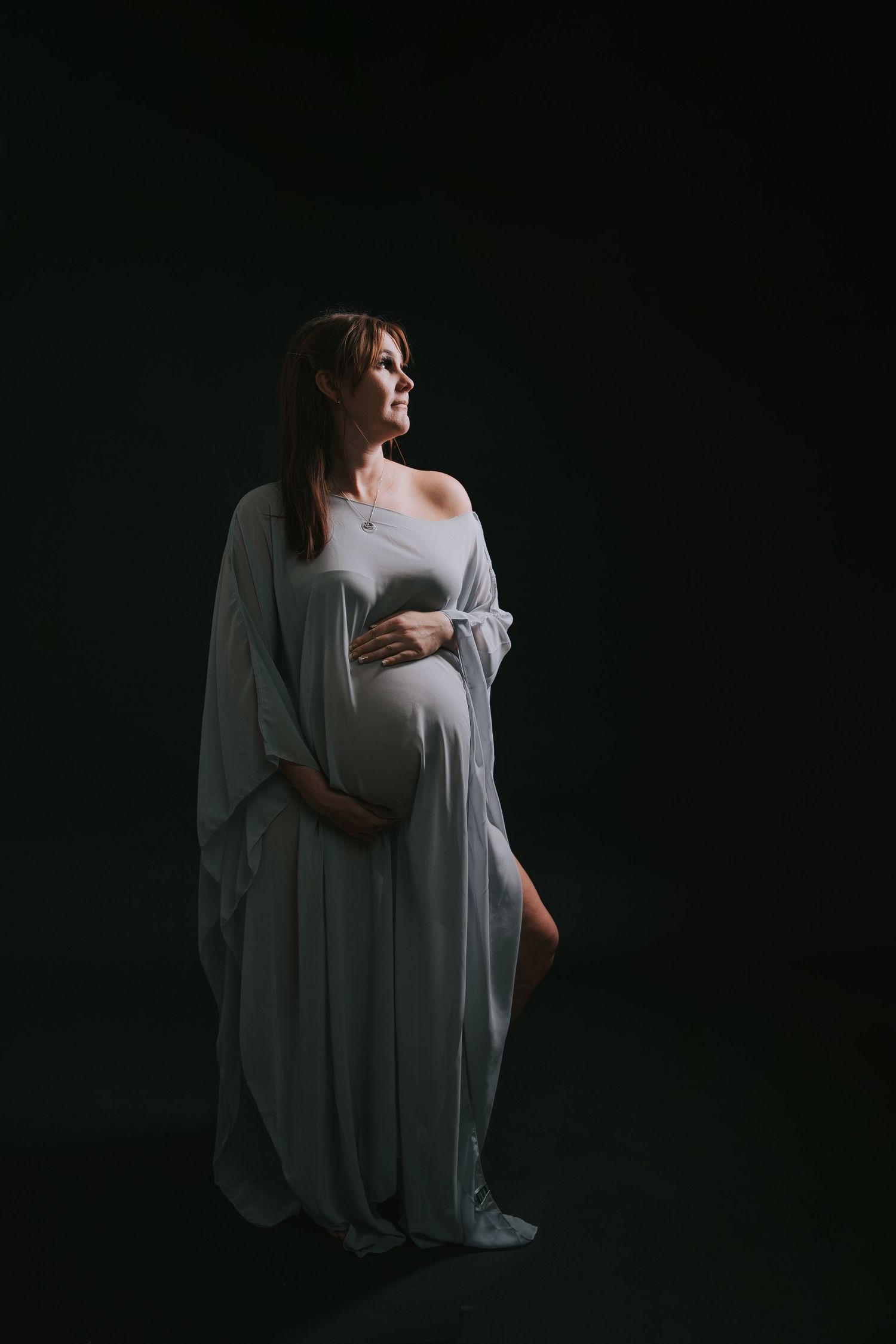 Dramatic low-key maternity portraits in grey against dark background.