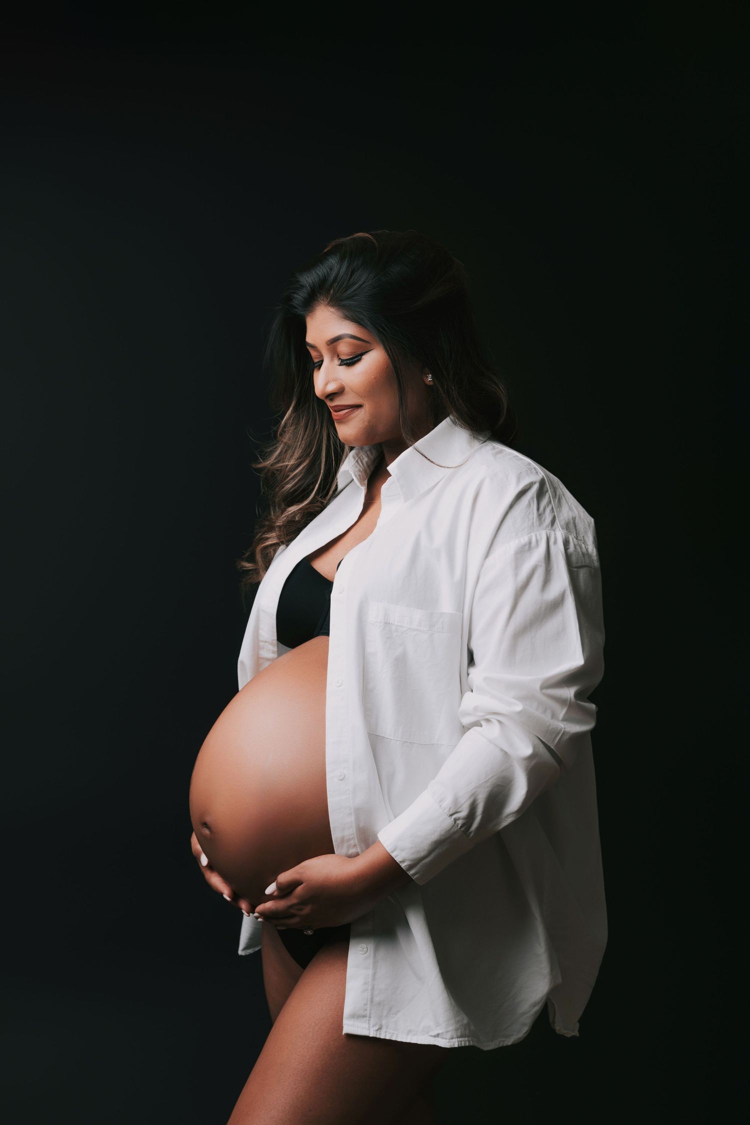 Minimalist maternity photos with white button-down shirt against dark background.