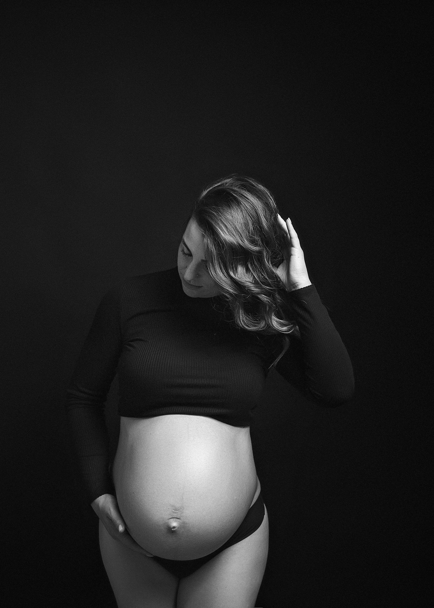 Black and white artistic maternity photos showing silhouette of pregnant belly against dark background.